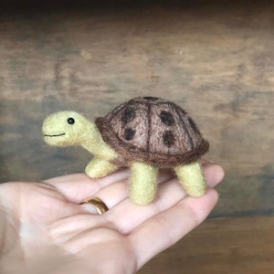 May include: A small, hand-felted turtle with a brown shell and yellow legs. The shell has a pattern of brown spots.