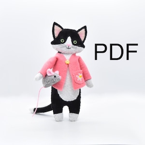 Könnte beinhalten: Eine schwarz-weiße Filzkatze trägt einen rosa Cardigan mit einer weißen gestickten Margerite auf der Tasche. Die Katze hält eine graue Filzmaus in ihrer Pfote. Das Wort "PDF" ist in schwarzen Buchstaben auf weißem Hintergrund in der oberen rechten Ecke des Bildes gedruckt.