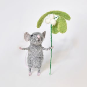 Könnte beinhalten: Eine handgefertigte Filzmausfigur in Grau, die einen Mistelzweig mit grünen Blättern und weißen Beeren hält. Die Maus hat rosa Ohren, Nase und Füße. Die Figur steht vor einem weißen Hintergrund.