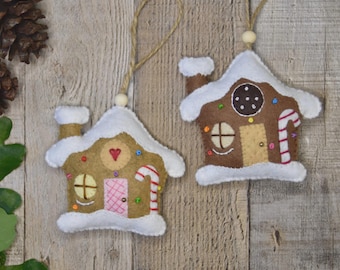 Pode incluir: Dois enfeites de feltro em forma de casa de gengibre, com acabamentos brancos semelhantes à neve e telhados castanhos. Cada casa tem um rebuçado, uma porta e detalhes coloridos. Penduram-se em fio com contas de madeira.