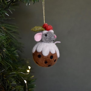 Peut inclure: Ornement de Noël fantaisiste représentant une souris en feutre sur un pudding marron. La souris a des poils gris, des oreilles roses et un chapeau de baies rouges et de feuilles de houx. Le pudding est décoré de glaçage blanc et de taches noires.