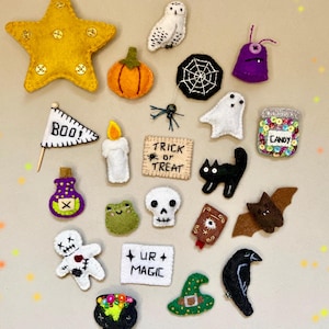 May include: A collection of felt Halloween-themed patches including a yellow star, pumpkin, owl, spider web, ghost, candy jar, BOO flag, candle, TRICK OR TREAT sign, black cat, potion bottle, frog, skull, bat, voodoo doll, UR MAGIC sign, cauldron, hat, and raven.