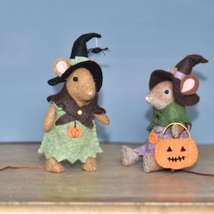 May include: Two handmade felt mice dressed in Halloween costumes. One mouse wears a witch hat and green dress with a pumpkin. The other mouse wears a witch hat and holds an orange pumpkin-shaped treat bag.