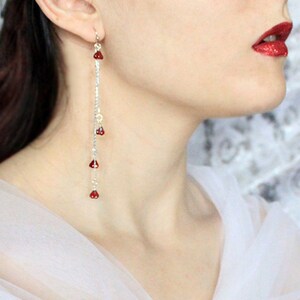 Peut inclure: Boucles d'oreilles longues en chaîne argentée avec des perles rouges en forme de goutte. Les boucles d'oreilles pendent du lobe de l'oreille.