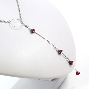 May include: A silver chain necklace with a circle pendant and dangling red beads.