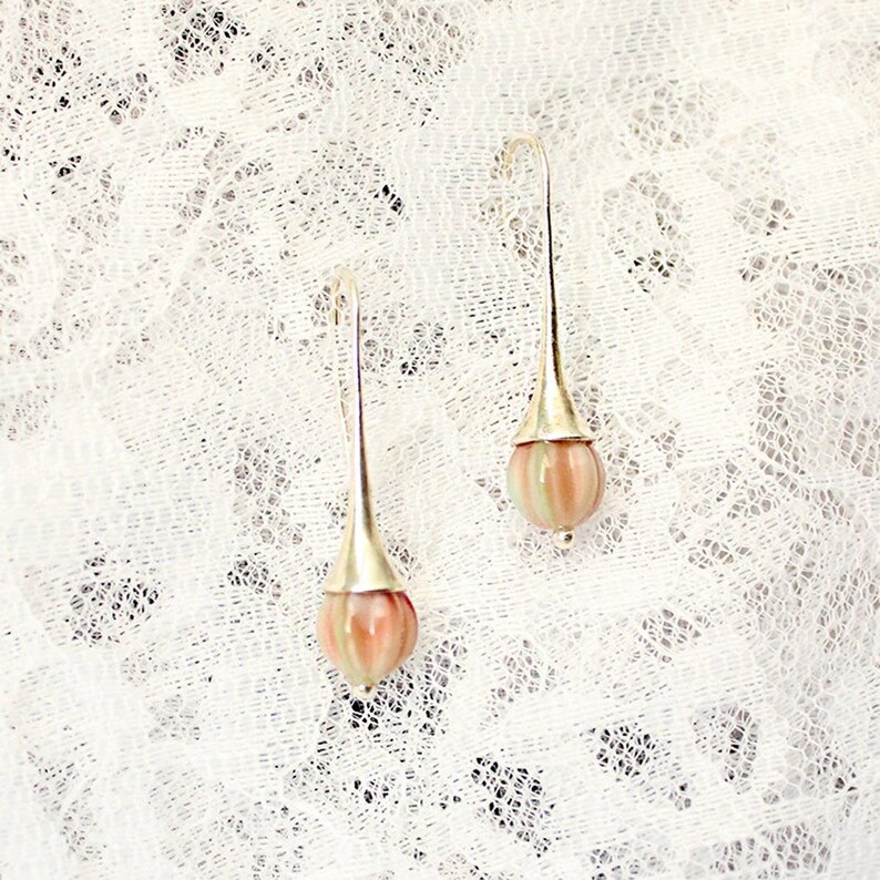 May include: A pair of silver dangle earrings with pink and white striped glass beads.