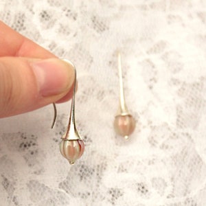 May include: A pair of silver dangle earrings with pink and white striped glass beads.