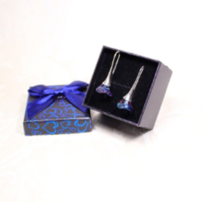 May include: A pair of blue and purple flower-shaped earrings in a black gift box with a blue ribbon. The earrings are silver and have a dangling design.