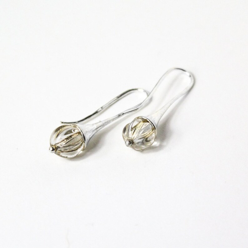 May include: A pair of silver dangle earrings with clear faceted glass beads. The beads are encased in a silver setting that resembles a flower bud.