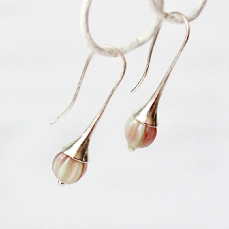 May include: A pair of silver dangle earrings with pink and white striped glass teardrop-shaped beads.