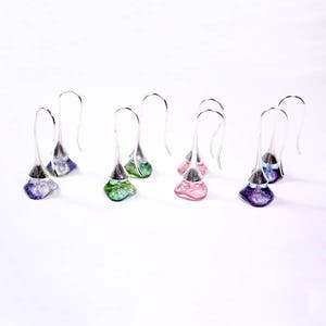 May include: Six pairs of silver dangle earrings with glass teardrop-shaped charms. The charms are in shades of purple, pink, and green.