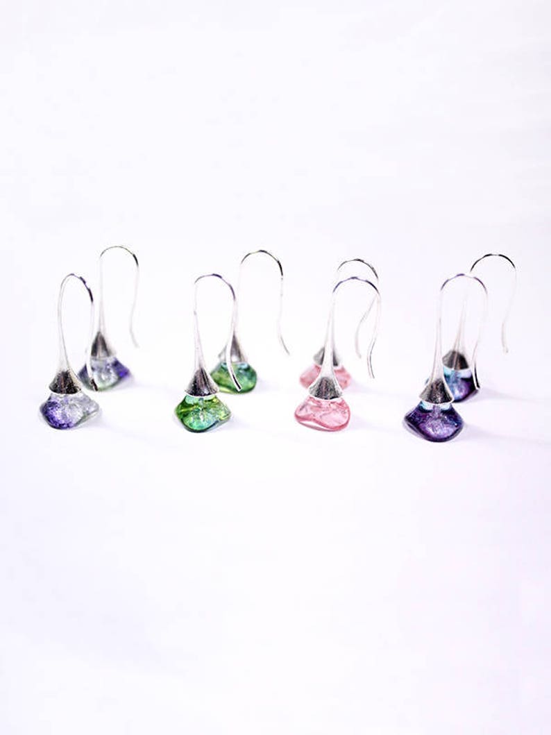 May include: Six pairs of silver dangle earrings with glass teardrop-shaped charms. The charms are in shades of purple, pink, and green.
