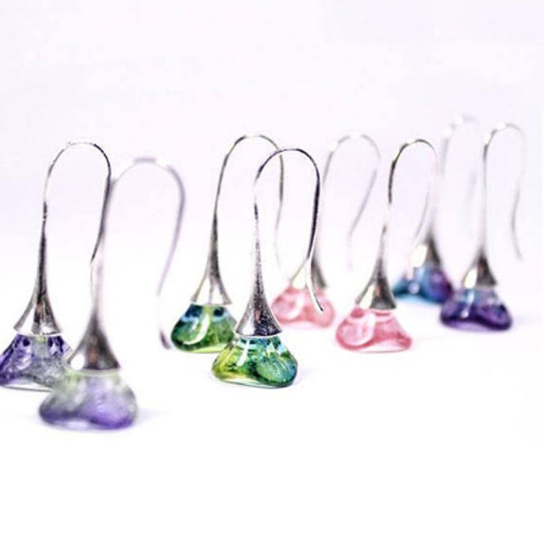 May include: A set of silver dangle earrings with colorful glass teardrop-shaped charms. The charms are in shades of purple, green, pink, and blue.