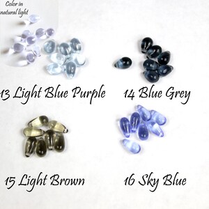 May include: Assortment of glass beads in various shades of blue, purple, brown, and grey. The beads are teardrop shaped and arranged in groups of 8-10 beads. The text "Color in natural light" is at the top of the image. The text "13 Light Blue Purple", "14 Blue Grey", "15 Light Brown", and "16 Sky Blue" are below each group of beads.