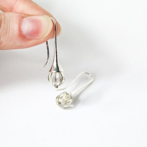 May include: A pair of silver dangle earrings with clear glass teardrop-shaped beads. The beads have a cage-like design.