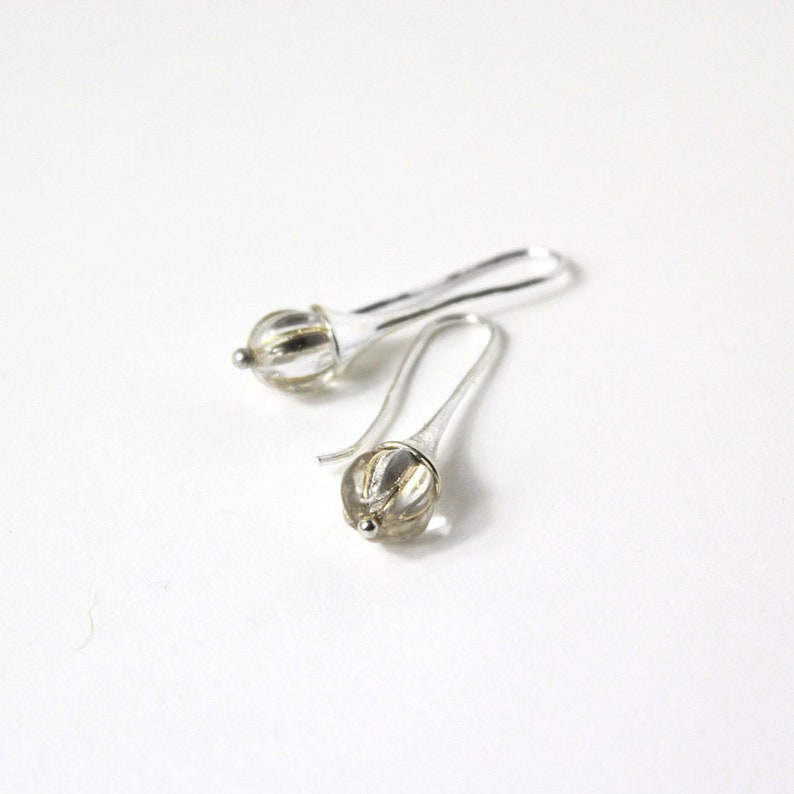 May include: A pair of silver dangle earrings with clear glass teardrop-shaped beads. The beads have a textured, ribbed surface.