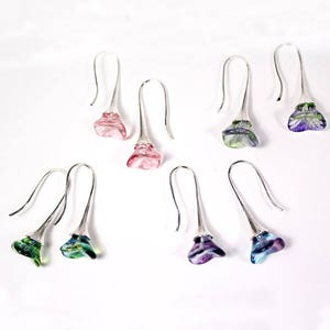 May include: Six pairs of dangle earrings with silver hooks and colorful glass flower-shaped charms. The charms are in shades of pink, green, blue, and purple.