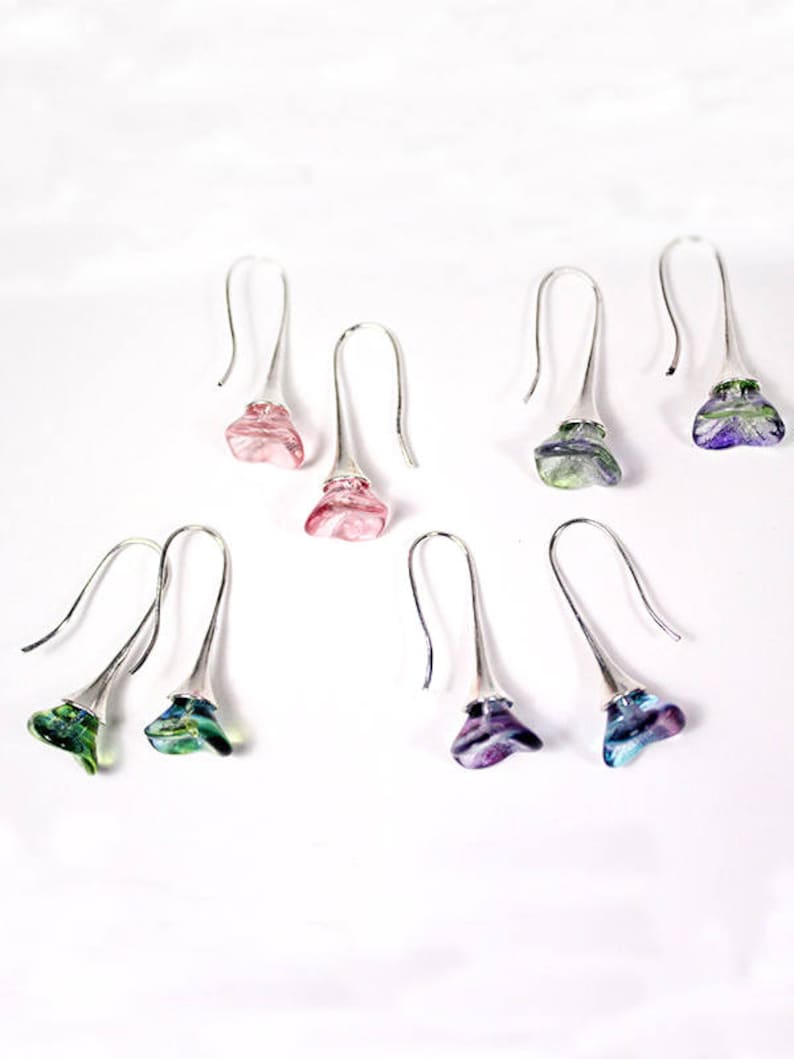 May include: Six pairs of dangle earrings with silver hooks and colorful glass flower-shaped charms. The charms are in shades of pink, green, blue, and purple.