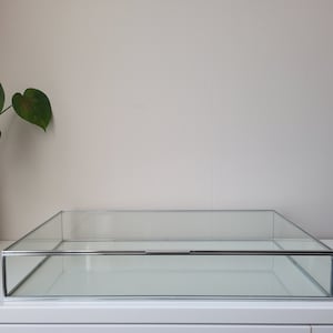 Może przedstawiać: Przezroczysta gablota ze szkła z srebrną metalową ramą. Gablota ma przesuwany daszek i stoi na białym tle.