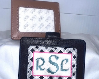 May include: Two leather cardholders. The top one is tan, and the bottom one is black. The black cardholder has a cross-stitch design with the initials "RSC" in teal, framed by a pink border and a black and white houndstooth pattern.