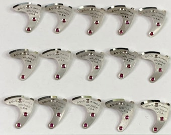 Könnte beinhalten: Nahaufnahme von 12 silbernen Uhrenteilen mit dem Text "6/0-D 17 JEWELS WALTHAM USA" auf jedem Teil. Die Teile sind in vier Reihen zu je drei angeordnet. Ein Lineal ist am unteren Rand des Bildes sichtbar.