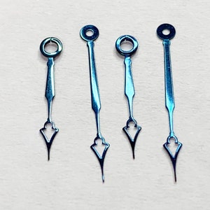 May include: Four blue metal watch hands with a pointed tip and a circular opening at the top. The hands are arranged in a row on a white surface.