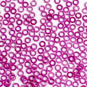 May include: A large quantity of small, pink, transparent, ring-shaped beads. The beads are scattered on a white surface.