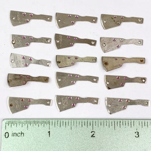 May include: A collection of 15 silver-colored watch parts with pink jewels. Each part has a different number and text printed on it. The parts are arranged in three rows of five. A ruler is included for scale.