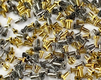 May include: A large collection of small, gold and silver gears. The gears are all different sizes and shapes, and they are scattered randomly on a white surface.