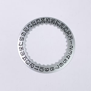 May include: A silver-coloured watch bezel with black numbers from 1 to 31 around the edge.