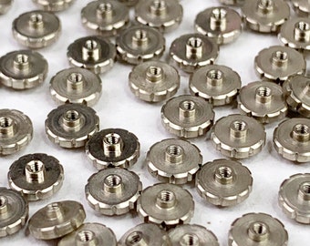 May include: A close-up view of a large quantity of silver-toned metal watch parts. The parts are small, round, and have a raised, textured edge. They are scattered on a white surface.