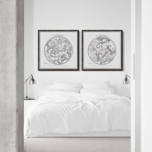 Könnte beinhalten: Zwei schwarze gerahmte Drucke von Vintage-Sternenkarten, mit dem Text "Die Sternbilder der nördlichen Hemisphäre" und "Die Sternbilder der südlichen Hemisphäre" über jeder Karte. Die Drucke hängen an einer weißen Wand über einem weißen Bett mit weißer Bettwäsche.