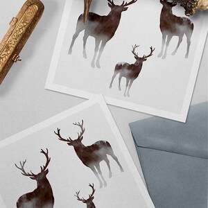 Puede incluir: Cuatro im&aacute;genes de silueta de ciervos con un fondo de bosque brumoso impresas en tarjetas blancas. Las tarjetas est&aacute;n dispuestas sobre una superficie gris con una caja decorativa dorada y una cornamenta marr&oacute;n.