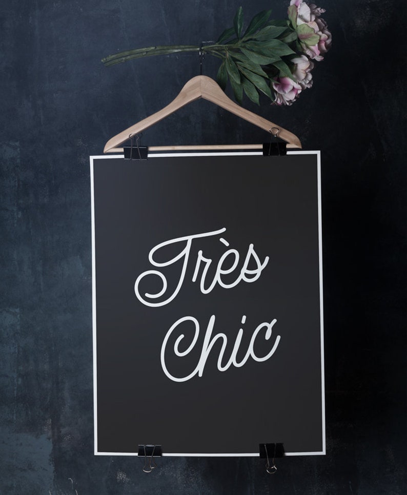 May include: A black and white poster with the text "Tr&egrave;s Chic" hanging on a wooden hanger against a dark blue background.
