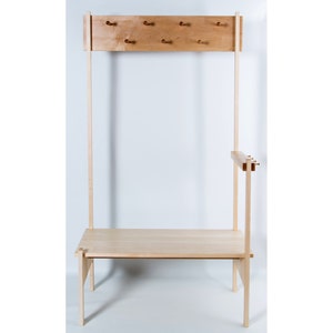 Peut inclure: Un portant en bois clair avec un banc, des supports verticaux et une section supérieure avec six chevilles pour suspendre des articles. Le design est minimaliste et moderne, adapté aux entrées ou aux chambres. Le banc mesure environ 122 cm de long.