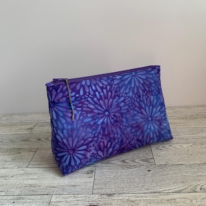 May include: Purple zippered pouch with a floral pattern. The pouch has a blue and purple batik design with a beaded zipper pull.