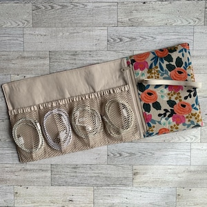 May include: A beige zippered pouch with a floral print on the outside. The pouch has multiple mesh pockets on the inside, each holding a white cord.