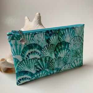 May include: A light blue zippered pouch with a seashell pattern and a silver seashell charm. The pouch is made of fabric and has a white background.