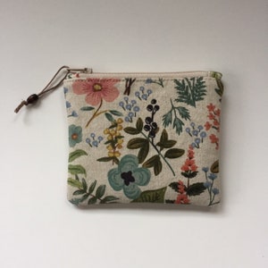 May include: A small zippered pouch with a floral print. The pouch is made of a beige fabric with a variety of flowers and leaves in shades of pink, blue, green, and yellow.