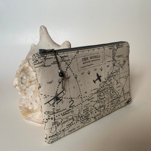 May include: A beige canvas zippered pouch with a world map print and a black airplane graphic. The text "THE WORLD MERCATOR PROJECTION" is printed on the pouch.