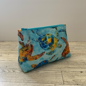 May include: A blue zippered pouch with a sea turtle print. The pouch has a silver charm attached to the zipper.
