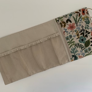 May include: A beige zippered pouch with a floral print on one side and a mesh pocket on the other side. The pouch has a handle and is designed to hold multiple items.