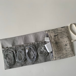 May include: A gray and beige travel organizer with multiple mesh pockets for storing cords and chargers. The organizer has a zipper closure and a map-like design on the outside.
