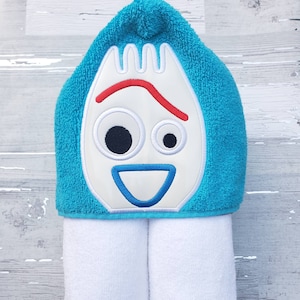 May include: A turquoise hooded towel with a white embroidered face of the character Woody from the Toy Story movie franchise. The towel is rolled up and the hood is folded down.