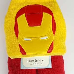 May include: Yellow hooded towel with a red and yellow Iron Man face embroidered on the hood. The towel is folded and has a red towel underneath. The label reads "Joyful Bundles JoyfulBundles.Etsy.com"