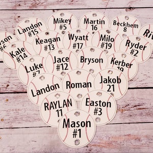May include: A collection of white baseball-themed tags with black text. Each tag has a name and a number. The tags are arranged in a random pattern on a wooden surface.