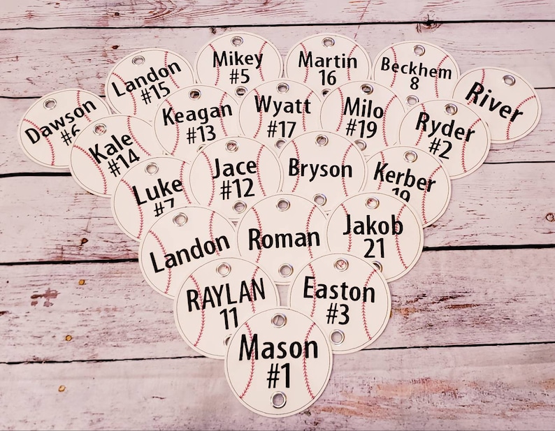 May include: A collection of white baseball-themed tags with black text. Each tag has a name and a number. The tags are arranged in a random pattern on a wooden surface.