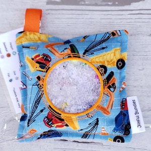 May include: A blue sensory toy with a clear plastic window filled with white beads. The toy is decorated with a construction theme and has the text "Joyful Bundles" on a white tag.