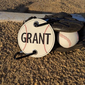 May include: White baseball-shaped tag with black stitching and the name "GRANT" embroidered in black. The tag has a black carabiner clip attached.