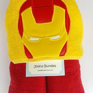 May include: Red and yellow hooded towel with an embroidered Iron Man face on the hood. The towel is folded and has a tag that says "Joyful Bundles JoyfulBundles.Etsy.com"